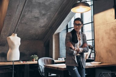 Başarılı moda tasarımcısı. Onu atölye masa üzerine eğilerek süre uzağa arıyorsunuz ve silah tutmak Eyewear ciddi genç kadın geçti