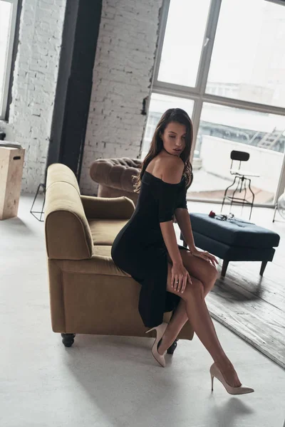 穿着黑色连衣裙的优雅女人在沙发上摆姿势 — 图库照片