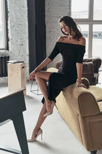 Модная Брюнетка Черном Элегантном Платье Позирует Себя Дома Рядом Диваном — стоковое фото