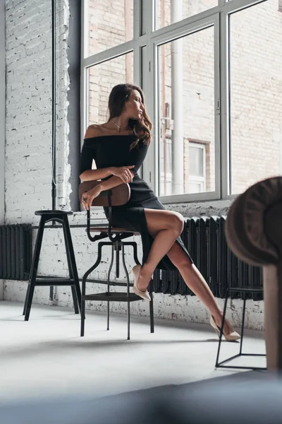 自宅の椅子に座ってエレガントな黒のドレスでブルネットの女性 — ストック写真