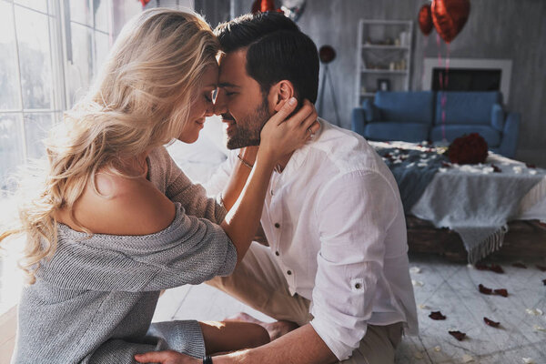Beautiful young couple bonding and smiling while sitting in bedroom, celebrating valentines day