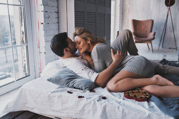Beautiful young couple embracing and kissing while lying on bed at home
