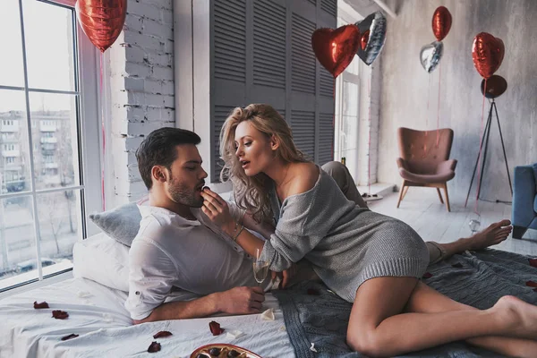 你应该试试看 美丽的年轻夫妇吃巧克力糖果和喝香槟 而躺在床上在家 — 图库照片