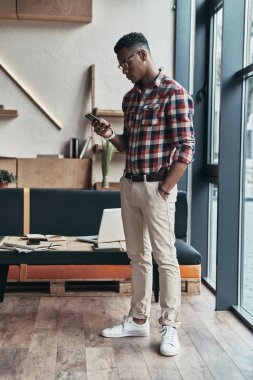 Cep telefonu kullaranarak ve modern ofis pencere, ayakta ciddi genç adam
