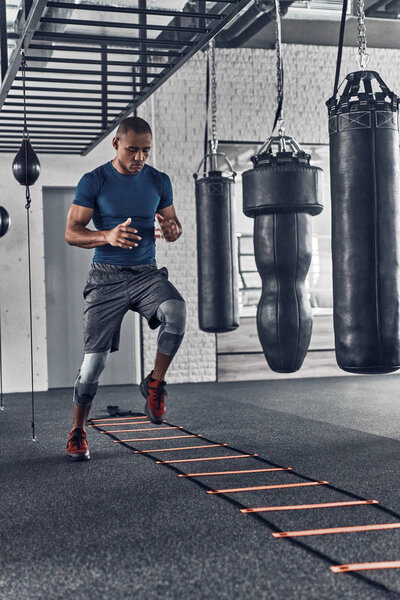 muscular young African man in sport clothing doing jumping exercise in gym