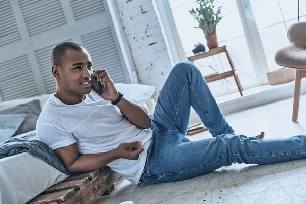 Bonito Jovem Africano Falando Telefone Enquanto Sentado Chão Casa — Fotografia de Stock