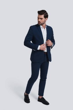 uzağa bakıyor ve onun ceket gri arka plan karşı dururken ayarlama tam takım yakışıklı genç adam tam uzunlukta