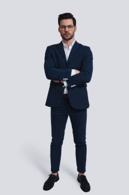 Kameraya bakarak ve silah tutmak tam takım kendine güvenen genç adam gri arka plan karşı dururken geçti