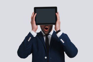 Dijital tablet ile yüz kapsayan ve ağız açık gri arka plan karşı dururken tutarak tam Takım şok genç adam