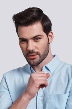 Kameraya bakarak ve gri arka plan karşı dururken gülümseyen çekici adam portresi