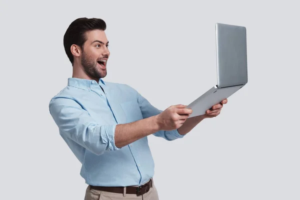 Szczęśliwy Młody Człowiek Trzyma Jego Laptop Uśmiechając Się Stojąc Szarym — Zdjęcie stockowe