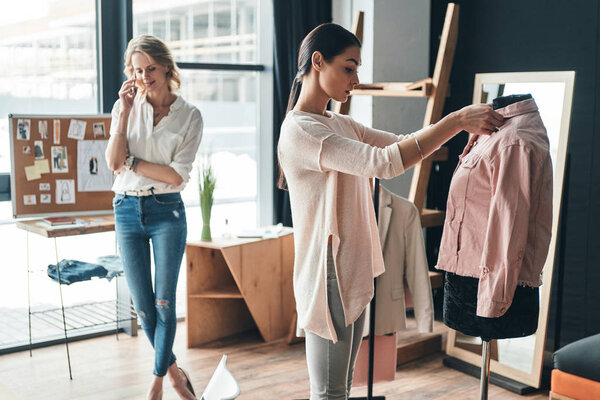 beautiful young woman talking on smart phone while brunette woman choosing clothes 