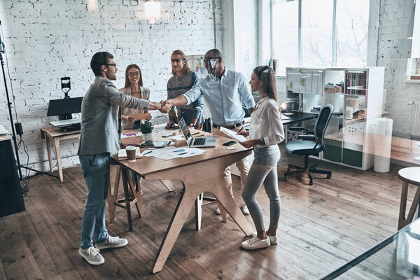 business men shaking hands at table in office board room with colleagues