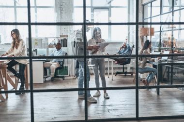 Kendinden emin ve başarılı takım. Çalışma ve birlikte yönetim kurulu odasında cam duvarın arkasında dururken iletişim modern gençlerin tam uzunlukta
