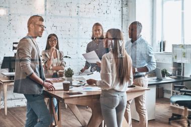 Takım yenilikçi. İş yaratıcı ofiste cam duvarın arkasında dururken tartışırken akıllı rahat kıyafet içinde modern gençlerin grup