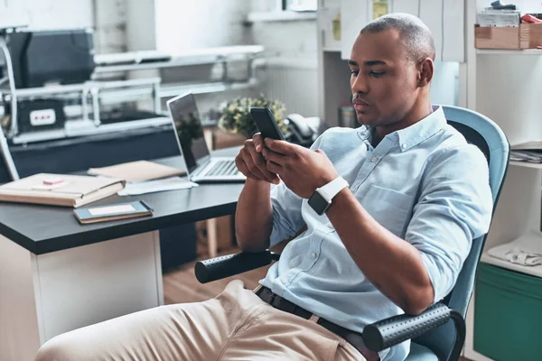 In touch with clients. Thoughtful young African man using smart phone while sitting in the office