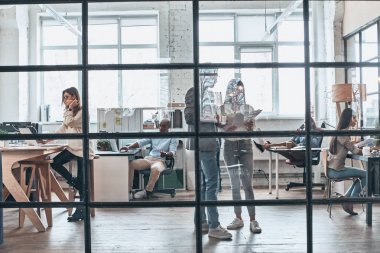 İlginç fikir paylaşımı. Çalışma ve birlikte yönetim kurulu odasında cam duvarın arkasında dururken iletişim modern gençlerin tam uzunlukta