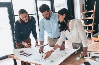 Taze fikirler için birlikte arama. Kendine güvenen genç iş adamları ofis planı süre gösteren bir şey tartışırken Üstten Görünüm