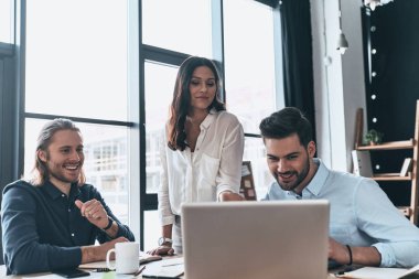 Önemli bir toplantı. Akıllı rahat kıyafet laptop işaret ve meslektaşları yaratıcı Office ile çalışırken gülümseyen genç modern kadın