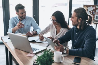 Kendi proje hakkında tutkulu. Smart casual modern gençlerin grup giymek birlikte çalışan ve yaratıcı ofiste otururken gülümseyen