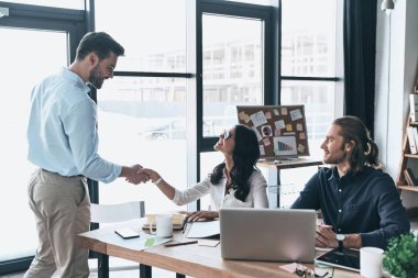 Sizinle çalışmak güzel. Genç modern iş arkadaşları el sıkışan ve yaratıcı ofiste otururken gülümseyen akıllı rahat kıyafet