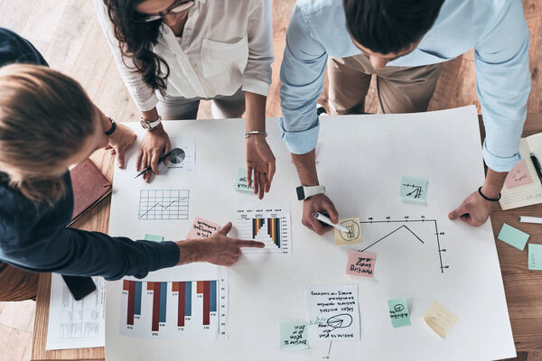 Going over details. Close up top view of young confident business people working together while man writing on blueprint in the office