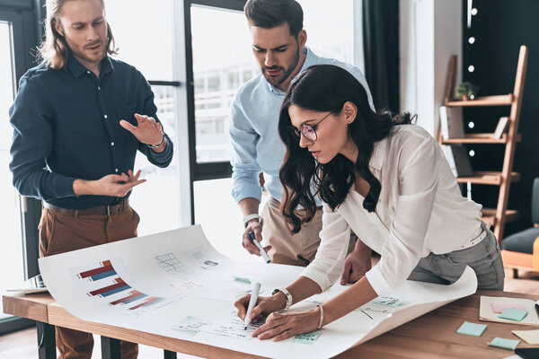 Planning new business strategy. Group of young confident business people discussing something while woman writing on blueprint in the office