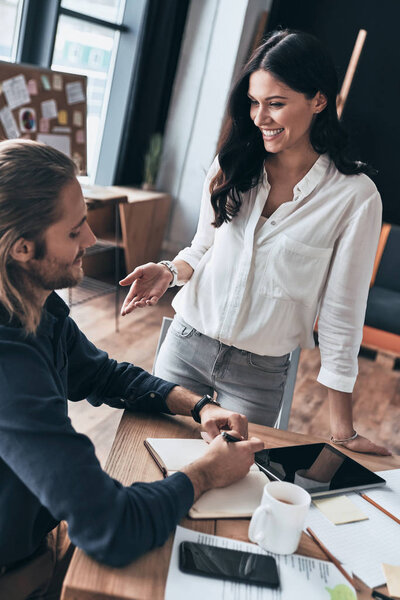 Happy to work together. Top view of young modern woman in smart casual wear gesturing and smiling while working together with colleague in the office