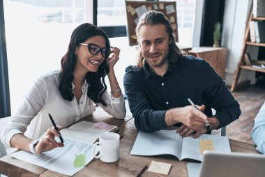 Kendi proje hakkında tutkulu. Üstten Görünüm içinde smart casual modern gençlerin giyim laptop işaret ve yaratıcı ofiste otururken gülümseyen