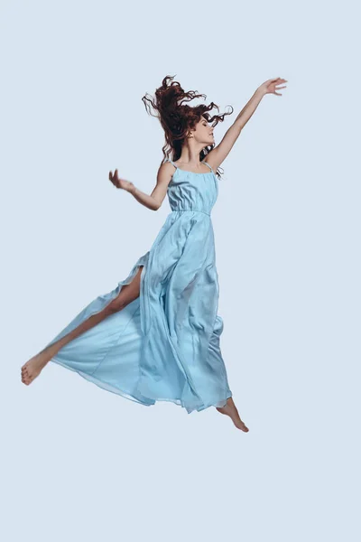 灰色の背景に対してホバリングしながらジェスチャー エレガントな青いドレスの魅力的な若い女性の完全な長さとスタジオ ショット — ストック写真