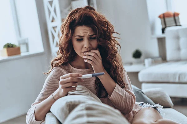 Mujer Joven Aterrorizada Mirando Prueba Embarazo Mientras Está Sentada Sofá —  Fotos de Stock