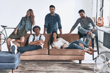 kanepede dinlenirken kameraya poz rahat kıyafet içinde şık gençlerin grup