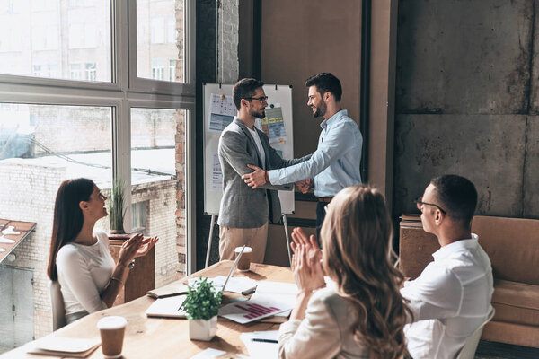 бизнесмены хлопают и улыбаются, а партнеры пожимают друг другу руки
 