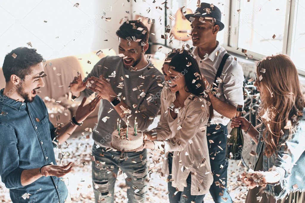 happy surprised man celebrating birthday with friends and cake in modern apartment with confetti