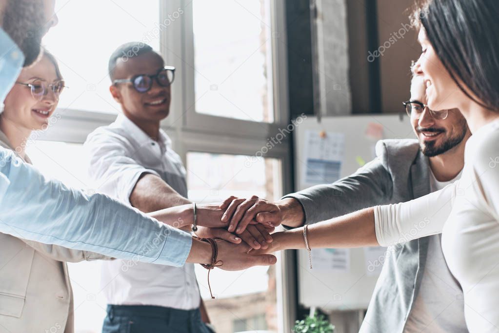 happy business team holding hands together in office room