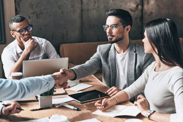 молодые бизнесмены за офисным столом пожимают друг другу руки
