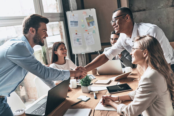 партнеры пожимают друг другу руки за столом в офисе
 