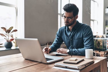 yakışıklı genç adam laptop ile masada otururken ders kitabı planı yazma