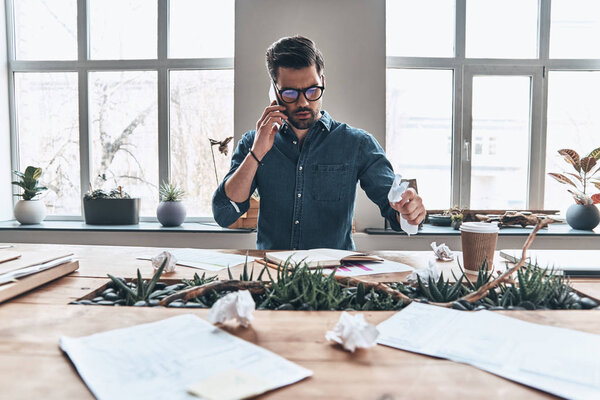handsome young man talking on smart phone and crumpling paper in office