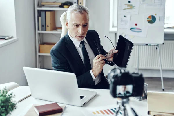 Senior man in elegant business suit using digital tablet while making social media video