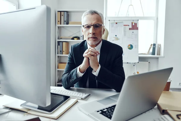 Homme âgé en costume d'affaires élégant utilisant des technologies modernes et regardant la caméra tout en travaillant dans un bureau moderne — Photo