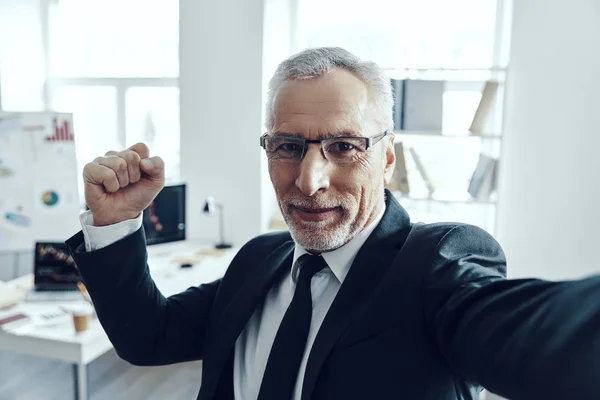 Självporträtt av senior man i elegant kostym tittar på kameran och ler stående i ämbetet — Stockfoto