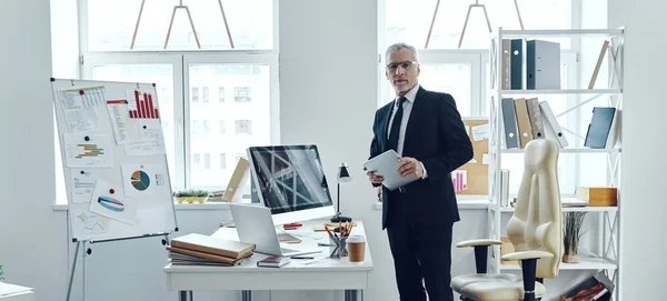 Comprimento total do comerciante sênior em terno de negócios elegante usando tablet digital enquanto trabalhava no escritório — Fotografia de Stock