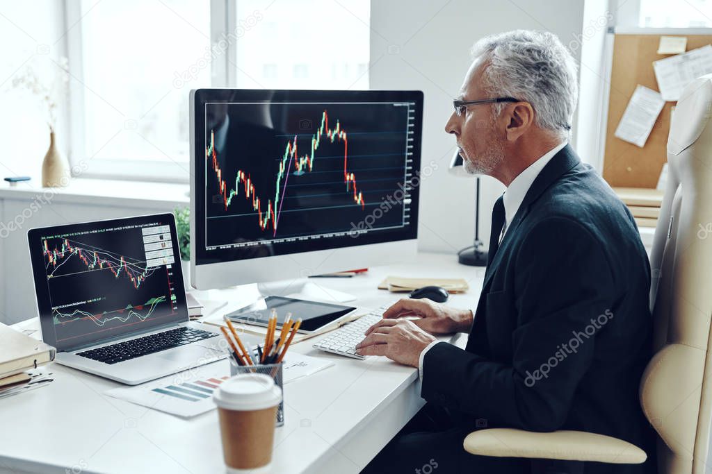 Senior trader in elegant business suit using computer while working at the office