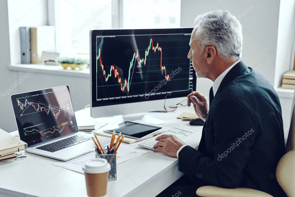 Senior trader in elegant business suit using computer while working at the office