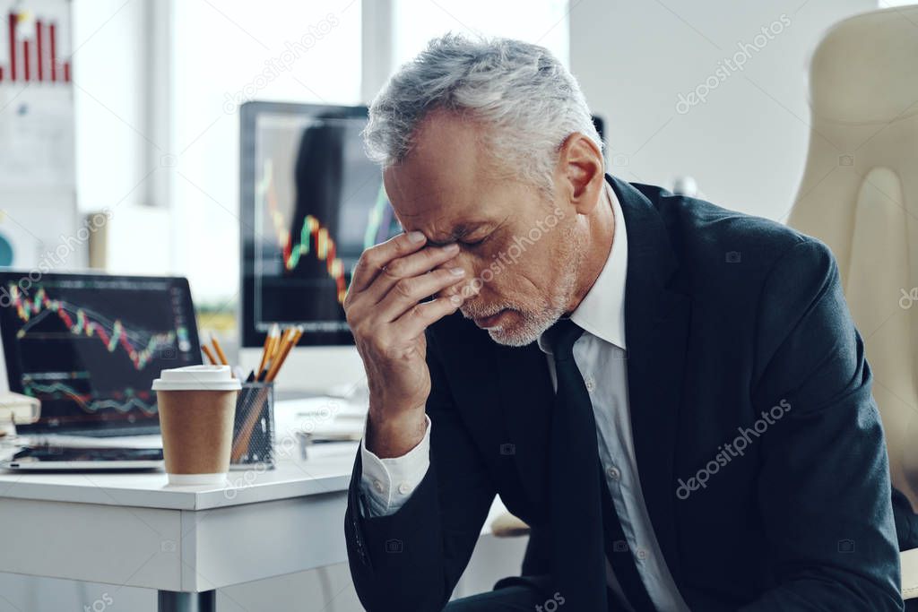 Frustrated senior man in elegant business suffering from headache while working at the office