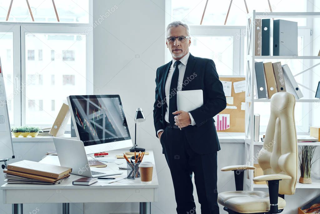Senior trader in elegant business suit using digital tablet while working at the office