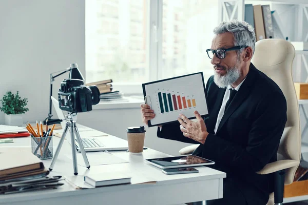 Homme mature confiant en costume élégant montrant le graphique et le partage d'expérience d'affaires tout en faisant de la vidéo sur les médias sociaux — Photo