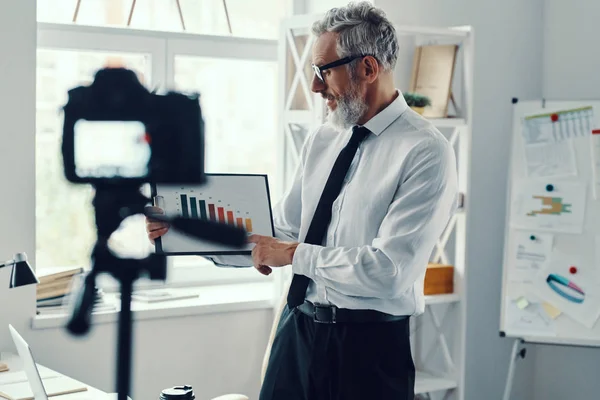 Sebevědomý dospělý muž v elegantní košili a kravatu ukazující graf a sdílení obchodních zkušeností při vytváření videa sociálních médií — Stock fotografie