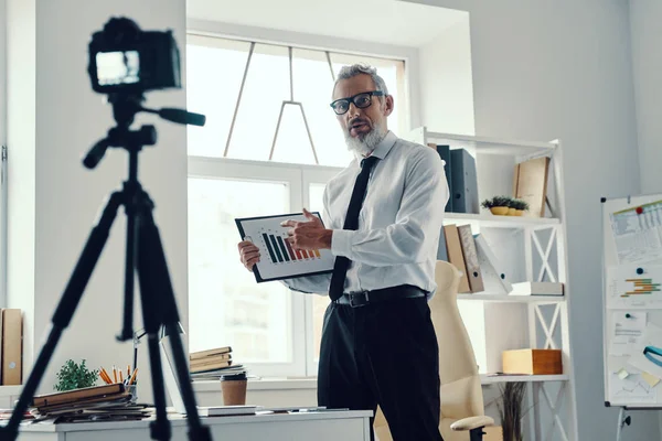 Sebevědomý dospělý muž v elegantní košili a kravatu ukazující graf a sdílení obchodních zkušeností při vytváření videa sociálních médií — Stock fotografie